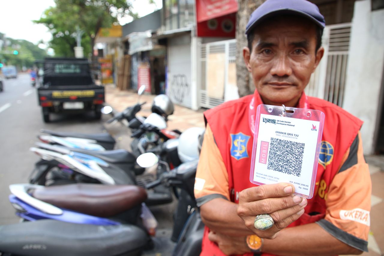 Pemerintah Kota (Pemkot) Surabaya melalui Dinas Perhubungan (Dishub) Kota Surabaya resmi memberlakukan pembayaran parkir non tunai dengan Qris mulai hari ini, Kamis (1/2/2024). Secara simbolis, peresmian pembayaran non tunai itu ditandai dengan pengalungan kode Qris oleh Kepala Dishub Kota Surabaya Tundjung Iswandaru kepada juru parkir di Jalan Tunjungan Surabaya. “Alhamdulillah hari ini kita memulai pembayaran parkir non tunai dengan Qris. Harapannya berjalan lancar,” kata Tundjung seusai meresmikan pembayaran parkir melalui Qris itu. Menurutnya, saat ini pihaknya menerapkan pembayaran parkir via Qris itu di 10 kawasan dengan 36 ruas jalan. Adapun 36 ruas jalan itu di antaranya adalah Jalan Tunjungan, Embong Malang, Bubutan, Jalan Semarang, Genteng, Blauran, Tanjunganom, Jalan Kedungdoro, Tidar, dan tempat lainnya. “Jadi, sekarang masih kita berlakukan di 36 ruas jalan. Sambil ini bertahap dan kita evaluasi terus. Targetnya seluruh jalan se Surabaya pakai Qris,” ujarnya. Ia juga menjelaskan bahwa saat ini baru 378 juru parkir (jukir) yang menerapkan pembayaran via Qris ini. Mereka ini adalah jukir-jukir yang sudah melengkapi administrasinya dalam pengurusan kode Qris. “Total ada 2.300 jukir dan semuanya ini bertahap, mereka tinggal melengkapi administrasinya lalu bisa menerapkan ini,” tegasnya. Sejauh ini, lanjut dia, memang masih ada beberapa pengguna yang belum paham tentang bayar parkir menggunakan Qris. Makanya, dalam rangka transisi dari pembayaran tunai ke pembayaran non tunai, Dishub Surabaya masih menfasilitasi warga dengan pembayaran tunai dan harus dengan karcis. “Jadi, di masa transisi ini masih bisa bayar tunai dan ada karcisnya. Tetapi selanjutnya sambil kita lakukan evaluasi untuk menggunakan Qris ini,” kata dia. Tundjung juga memastikan bahwa program pembayaran parkir dengan Qris ini sudah didukung oleh semua juru parkir se Kota Surabaya. Bahkan, ia juga memastikan bahwa program ini juga untuk meningkatkan PAD (Pendapatan Asli Daerah) Surabaya dan juga untuk meningkatkan kesejahteraan jukir. Sementara itu, Ketua Umum Paguyuban Juru Parkir Surabaya (PJS) Izul Fiqri memastikan seluruh jukir se Kota Surabaya sudah menyetujui penerapan pembayaran parkir melalui Qris itu. Meski begitu, persetujuannya itu dengan sejumlah catatan. “Catatan yang paling utama adalah kesejahteraan juru parkir Surabaya,” kata Izul saat ikut peresmian di Jalan Tunjungan. Ia juga memastikan bahwa paguyuban juru parkir itu sudah berkomitmen untuk mendukung program tersebut. Bahkan, ia juga mengakui sudah memberikan arahannya kepada seluruh juru parkir se Kota Surabaya untuk terus berkalung kode Qris. “Seluruh jukir se Surabaya kami pastikan berkalungkan Qris, sehingga masyarakat diberikan pilihan. Yang mau pakai Qris silahkan dan yang tidak siap dengan Qris silahkan pakai tunai dengan karcis. Ini tentu akan menjadi evaluasi kita ke depannya,” pungkasnya